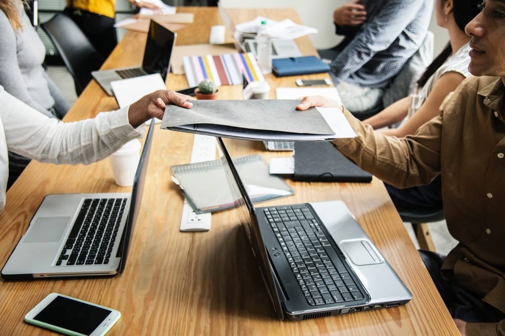 meeting table with laptops and people discussing